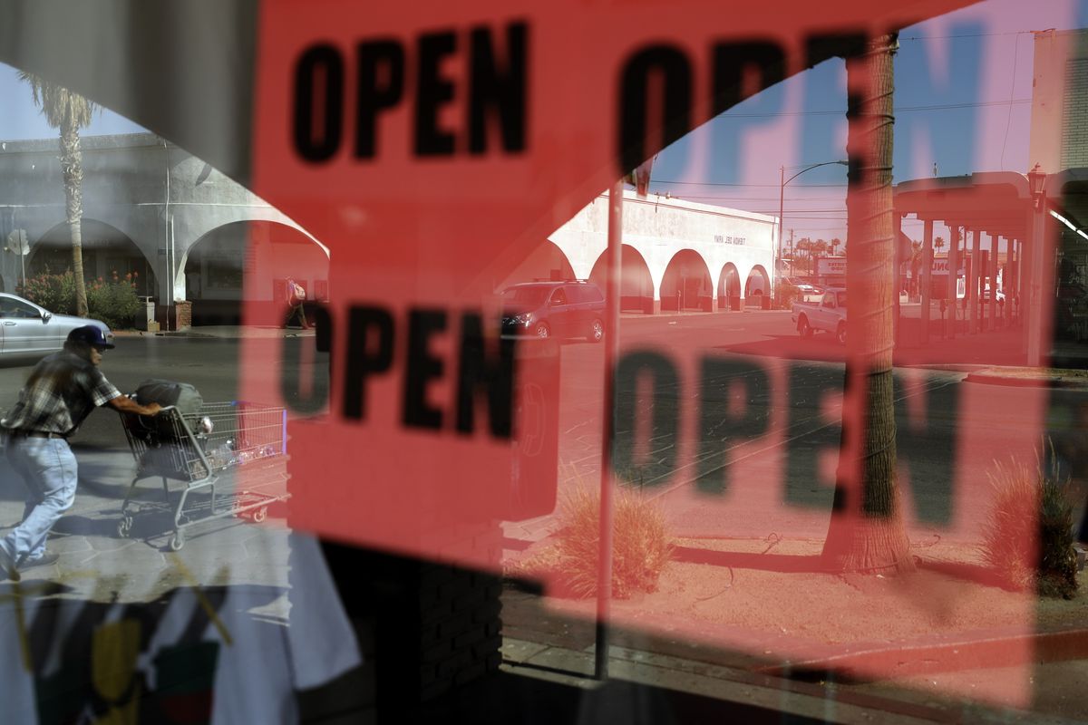 FILE - In this June 30, 2020, photo, a man passes a clothing shop with open signs in the window in Calexico, Calif. A year after the first coronavirus shutdowns, many U.S. states and cities are still struggling with a silent side effect: Public records have become harder to get. As states prepared to reopen their economies following coronavirus shutdowns last spring, The Associated Press asked governors across the U.S. for records that could shed light on how businesses and health officials influenced their decisions. (Gregory Bull)