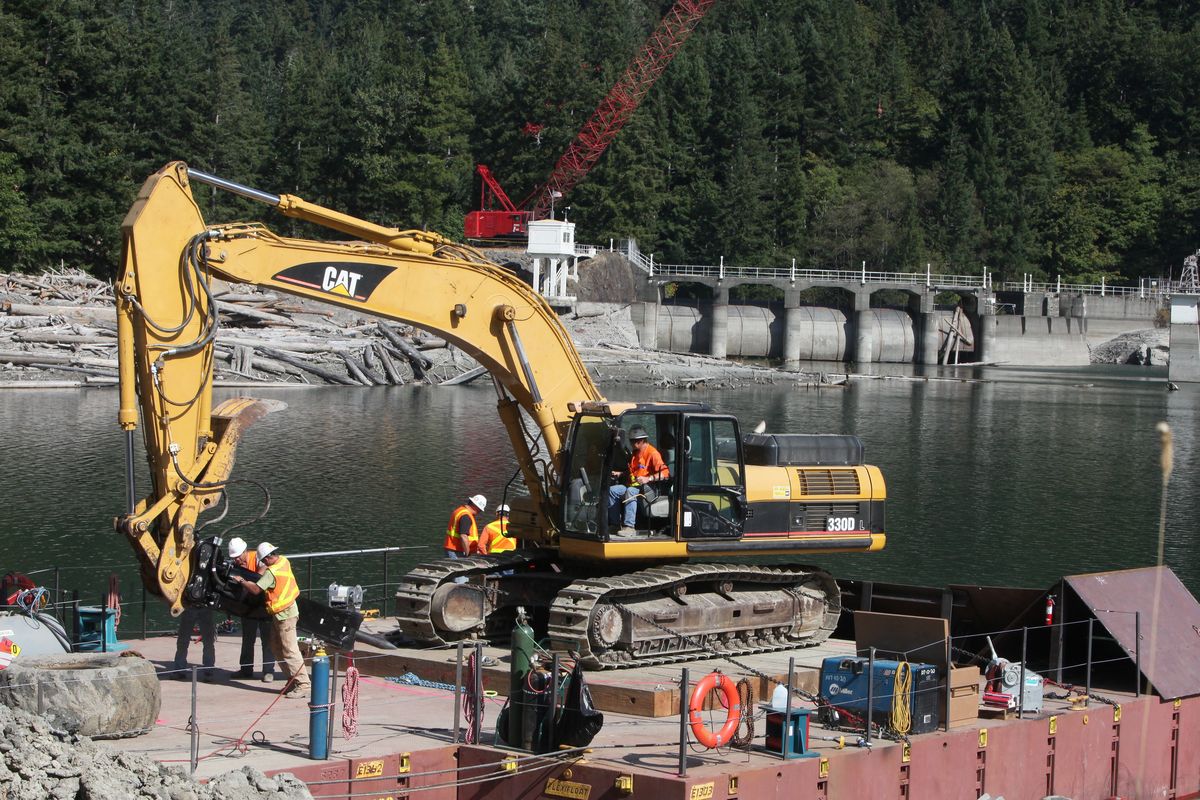 A construction crew on Thursday prepares a hydraulic hammer on a barge that was towed to Glines Canyon Dam to start the demolition of the structure. The first chunks of the dam hit the water Thursday. (STEVE RINGMAN)