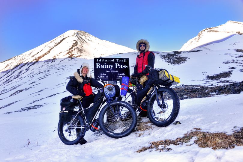 Two cyclists on fat bikes pause at Rainy Pass on the Iditarod Trail. They were traveling in February from Anchorage to Point Hope, a distance of about 1200 miles. The sign was installed by Josh Rindal and Bob Jones of Kettle Falls, who were snowmobiling 1,400-miles along the route of Alaska's famous race in March 2014. (Robert Jones)