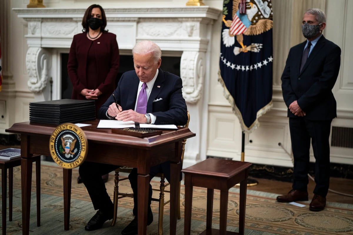 President Joe Biden, with Vice President Kamala Harris and Director of the National Institute of Allergy and Infectious Diseases Anthony S. Fauci by his side, signs executive orders after speaking about the pandemic in the State Dining Room at the White House on Jan. 21, 2021.  (Jabin Botsford/The Washington Post)