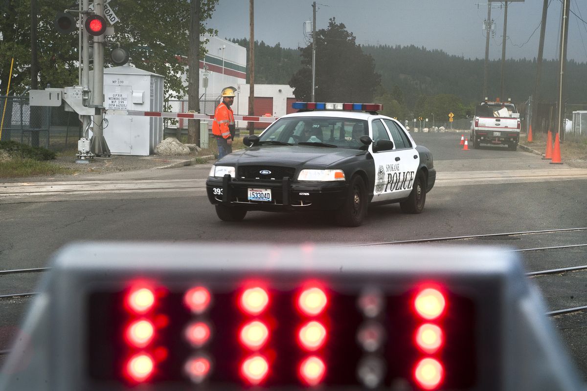 Spokane police officers are waved around railroad crossing arms by a Union Pacific employee Tuesday during construction on the tracks along Waterworks Street in Spokane. Emergency response vehicles were stopped at the same spot earlier this month by a train when responding to a plane crash in the Spokane River. (Dan Pelle)