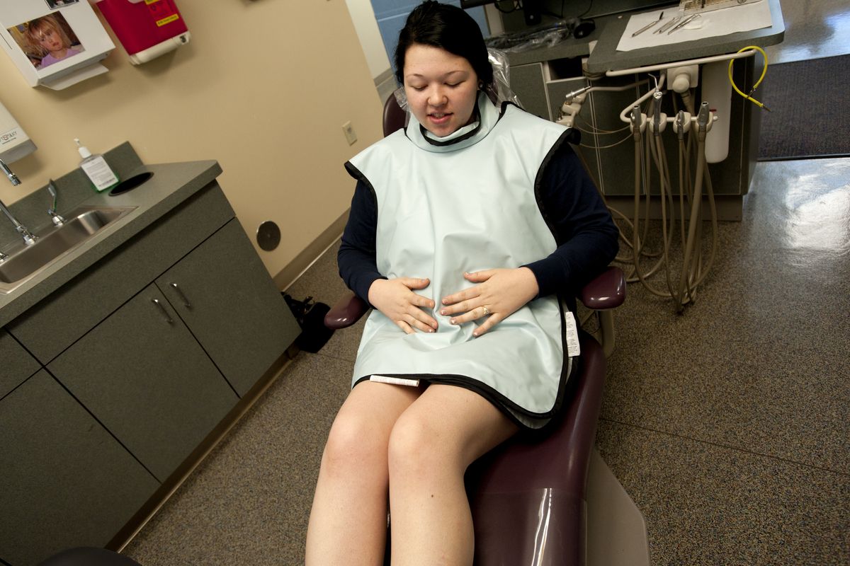 Mother-to-be Ashley Leon puts her hands on her stomach after a nurse fitted her with a dental lead apron to protect from radiation during tooth X-rays last week at CHAS dental clinic on Maple Street in Spokane. (Tyler Tjomsland)