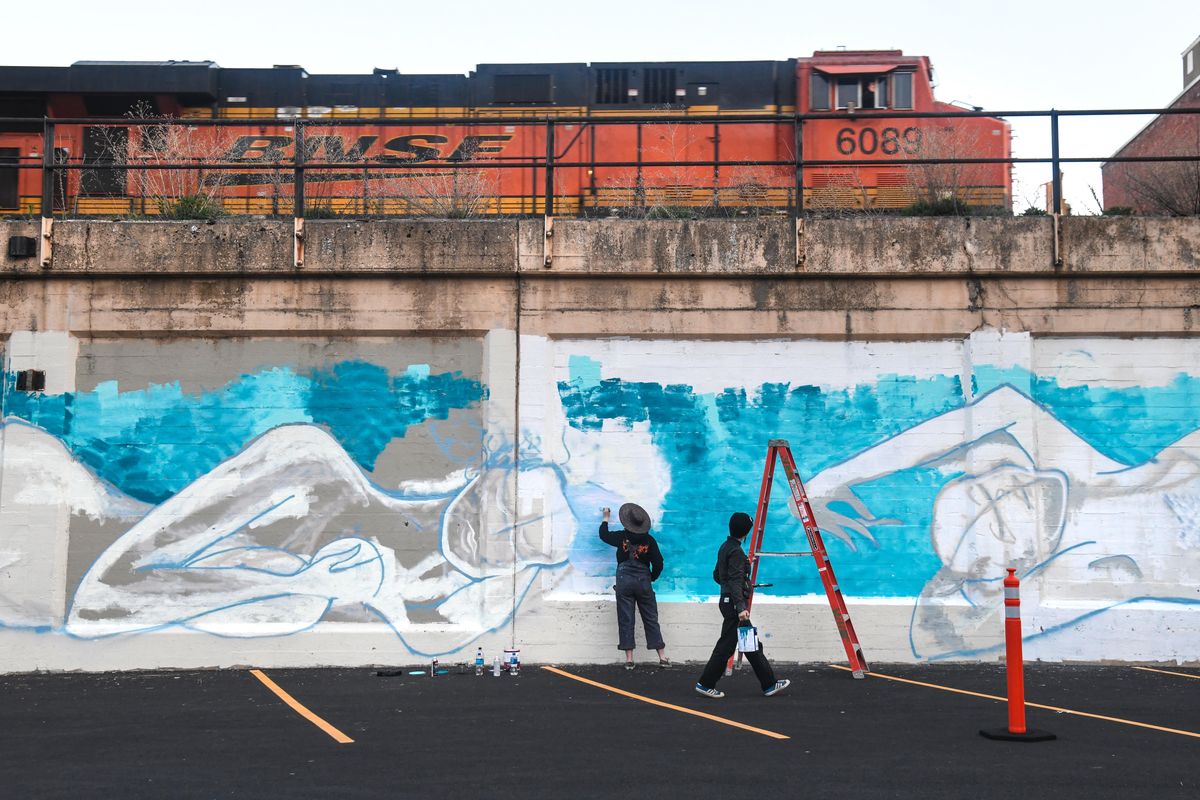 As a BNSF train passes as artists Shelby Allison and Susan Webber paint the bottom layer of their 160-foot mural, Wednesday, May 1, 2019, on Stevens Street just south of First Avenue in downtown Spokane. (Dan Pelle / The Spokesman-Review)