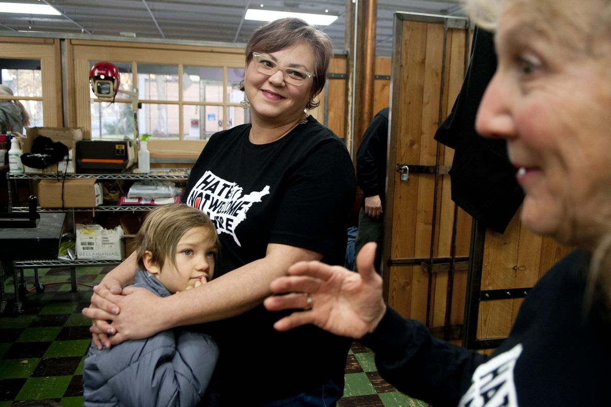 Randi Madison holds her daughter, Scarlett Jacobs, 7, as she listens to her former EWU professor, Barb Brock, talk about their “Hate Is Not Welcome Here”  merchandise at Ammonite Ink, in Spokane, on Wednesday, Nov. 29, 2017. The merchandise is in response to crimes against Norris Colley, a black man who was called racial slurs, threatened, and then shot at while at his home. (Kathy Plonka / The Spokesman-Review)