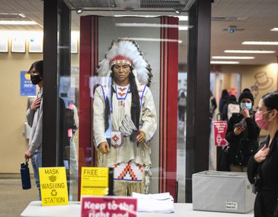 Students and a Spokane Public Schools administration member pause in the North Central High School hallway around the statue of a Native American male figure that served as the school’s mascot during the Pledge of Allegiance on the first day of in-person classes March 1. The school will now be changing its mascot.  (DAN PELLE/THE SPOKESMAN-REVIEW)