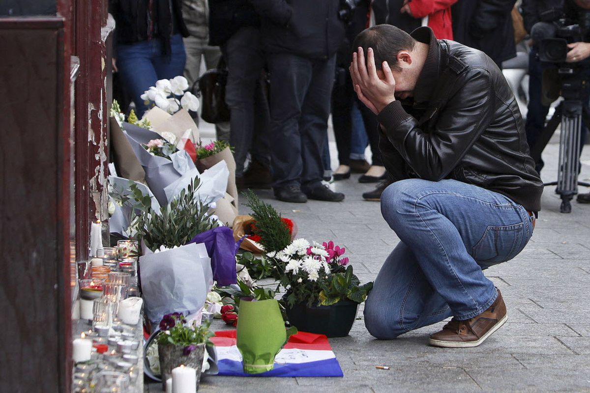 A man holds his head in his hands as he lays flowers in front of the Carillon cafe, in Paris, Saturday, Nov.14, 2015. French President Francois Hollande vowed to attack Islamic State without mercy as the jihadist group admitted responsibility Saturday for orchestrating the deadliest attacks inflicted on France since World War II. (Thibault Camus / Associated Press)