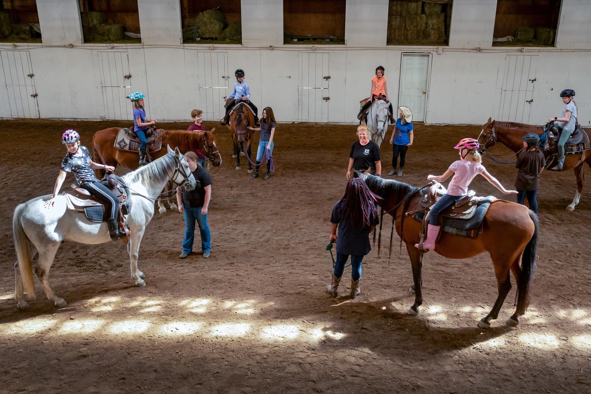 Michelle Zolezzi, center, gathers young riders and their side-walking assistants together for one last time during the final day of the Relational Riding Academy near Cheney, Friday, Aug. 23, 2019. Zolezzi, has about 25 campers at her weeklong camp who help around the school and help other children with riding lessons. (Colin Mulvany / The Spokesman-Review)