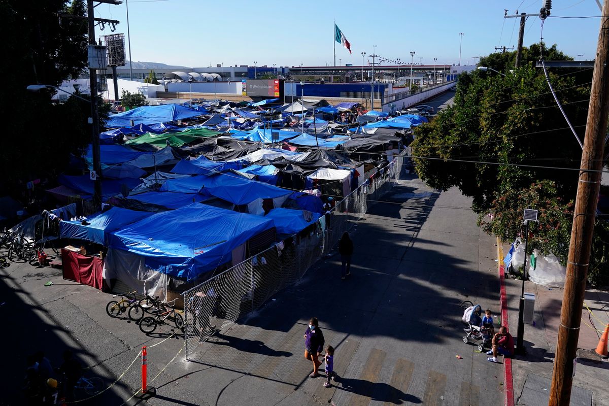 FILE - Migrants, below, walk outside a camp that blocks the entrance to a pedestrian crossing into the United States, above, Nov. 8, 2021, in Tijuana, Mexico. The encampment, now encircled in chain link fencing after an Oct. 28 operation by local police, is a temporary home for hundreds of migrants hoping to seek asylum in the United States.  (Gregory Bull)