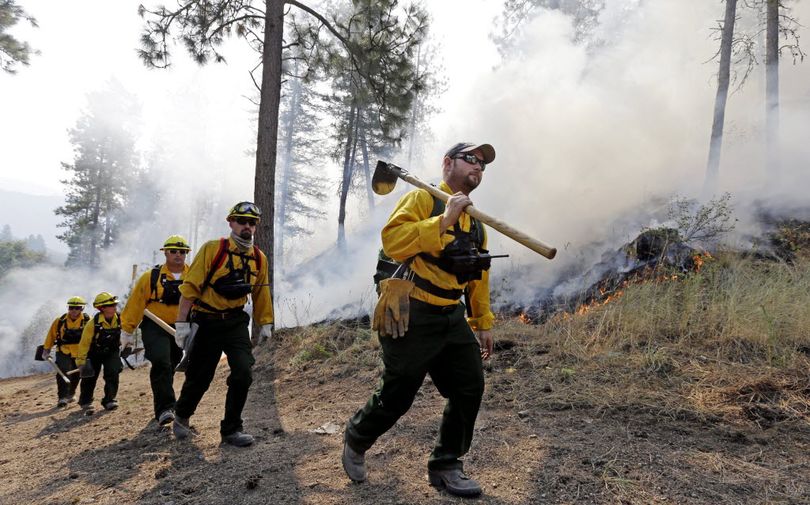 A group of firefighters head up a hill to keep an eye on an area burning between houses and the main fire Saturday, Aug. 22, 2015, in Okanogan, Wash. Out-of-control blazes in north-central Washington have destroyed buildings, but the situation is so chaotic that authorities have 
