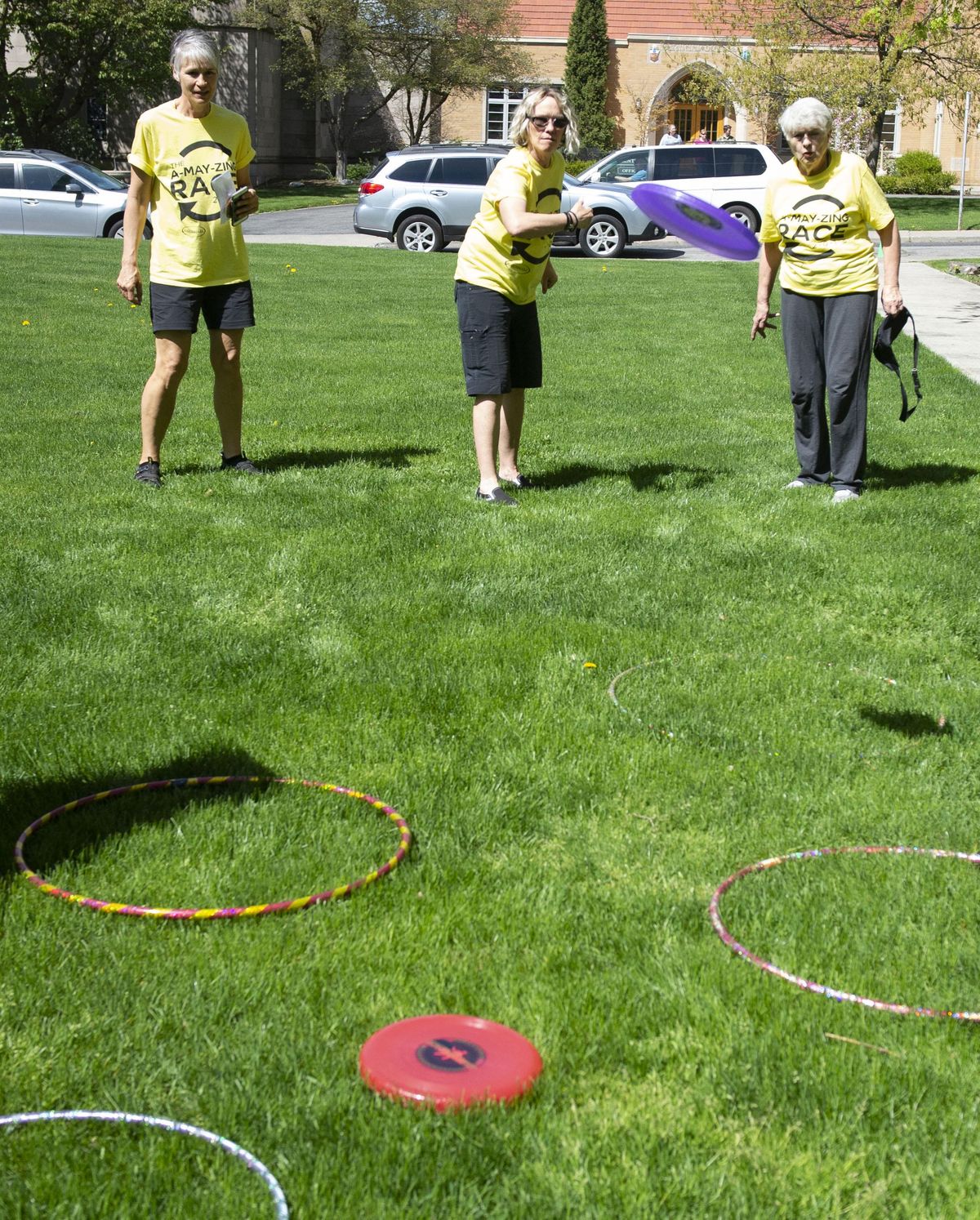 A-MAY-Zing Race participants, left to right, Cary Synder, Denise Bartlett and Touchmark resident Joanne McCann perform a task of tossing a flying disk into a ring behind Lindaman’s Gourmet-to-Go on May 4. (Colin Mulvany / The Spokesman-Review)