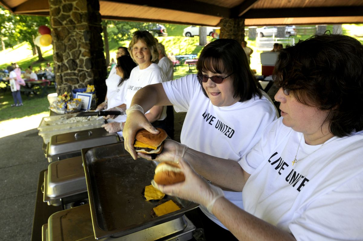 Volunteers Jo Ann Hagen, center, and her sister, Heidi Borders, right, dish up cheeseburgers for those attending the 50th anniversary celebration of Cancer Patient Care at Manito Park Saturday.  (Jesse Tinsley / The Spokesman-Review)