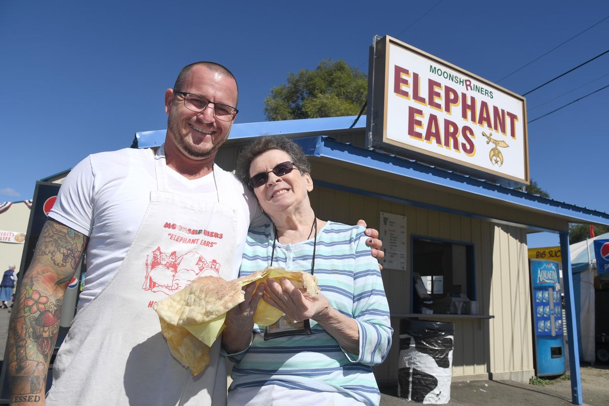 Gabe Thompson stands with Violet Hawkins as she munches on an elephant ear from the Shriners’ booth at the Spokane Interstate Fair Monday, Sept. 12, 2016. It was Hawkins who, more than 30 years ago, brought the idea for an elephant ear booth to the Shriners. Hawkins perfected the recipe and it’s still done the same way today. Thompson is part of a new generation of Shriners. The Shriners will have a booth at the fair again this year. (Jesse Tinsley / The Spokesman-Review)