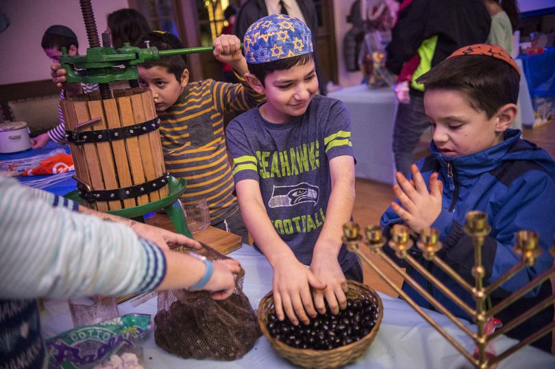 Left to right, Mendel Hahn checks out the olive press while Jacob Barenti and Collin Thiesen fill a bag with olives at Chabad of Spokane’s Chanukah Family Celebration on Dec. 26, 2016, at the Spokane Women's Club. Monika Wachowiak shows the boys how to make olive oil. (Liz Kishimoto / The Spokesman-Review)