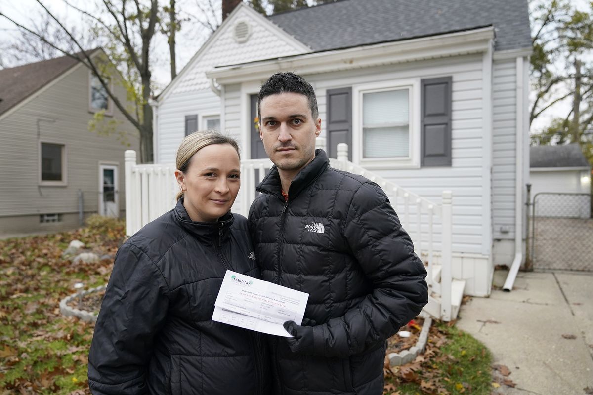 Nicole and Simon Obarto, holding a lead and copper analysis of water from the Oakland County Health Division, stand outside their home in Royal Oak, Mich., on Thursday, Nov. 18, 2021. The couple had their water line tested for lead and the results were high enough to have the lead service line replaced.  (Carlos Osorio)