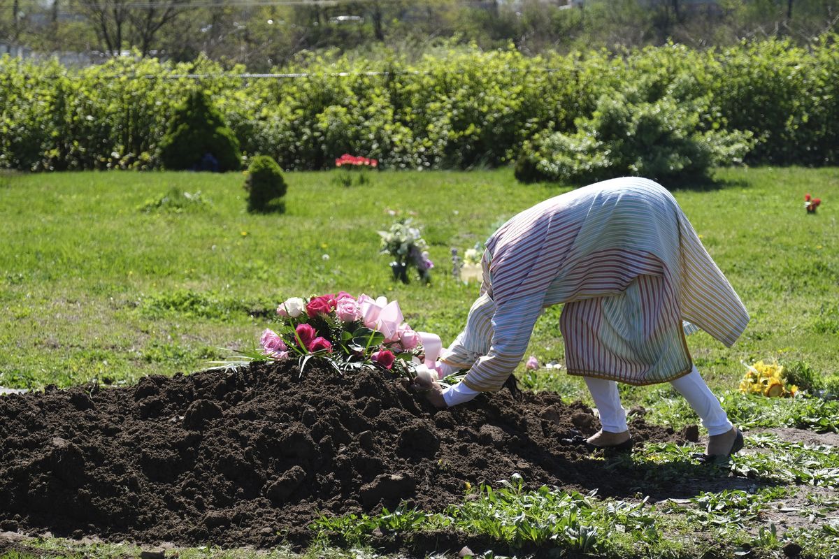 FILE - In this May 2, 2020, file photo, Erika Bermudez becomes emotional as she leans over the grave of her mother, Eudiana Smith, at Bayview Cemetery in Jersey City, N.J., Bermudez was not allowed to approach the gravesite until cemetery workers had buried her mother, who died of COVID-19. Other members of the family and friends stayed in their cars.  (Seth Wenig)