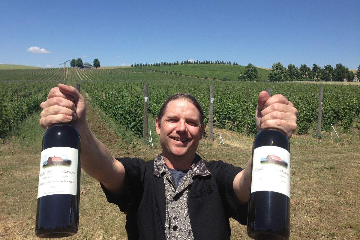 William VonMetzger, winemaker for Walla Walla Vintners, holds up two bottles of his award-winning wines in front of the winery’s estate vineyard east of Walla Walla, Wash. (Andy Perdue Great Northwest Wine)
