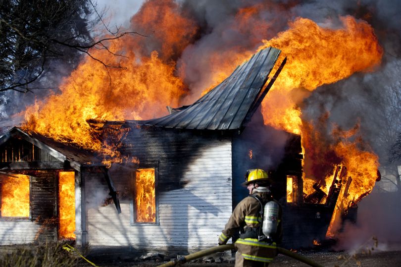 A firefighter with the Spokane Valley Fire Department hauls a hose Tuesday through the front yard of a house at 9621 E. Empire Ave. that was donated to the department for a training exercise. (Tyler Tjomsland)