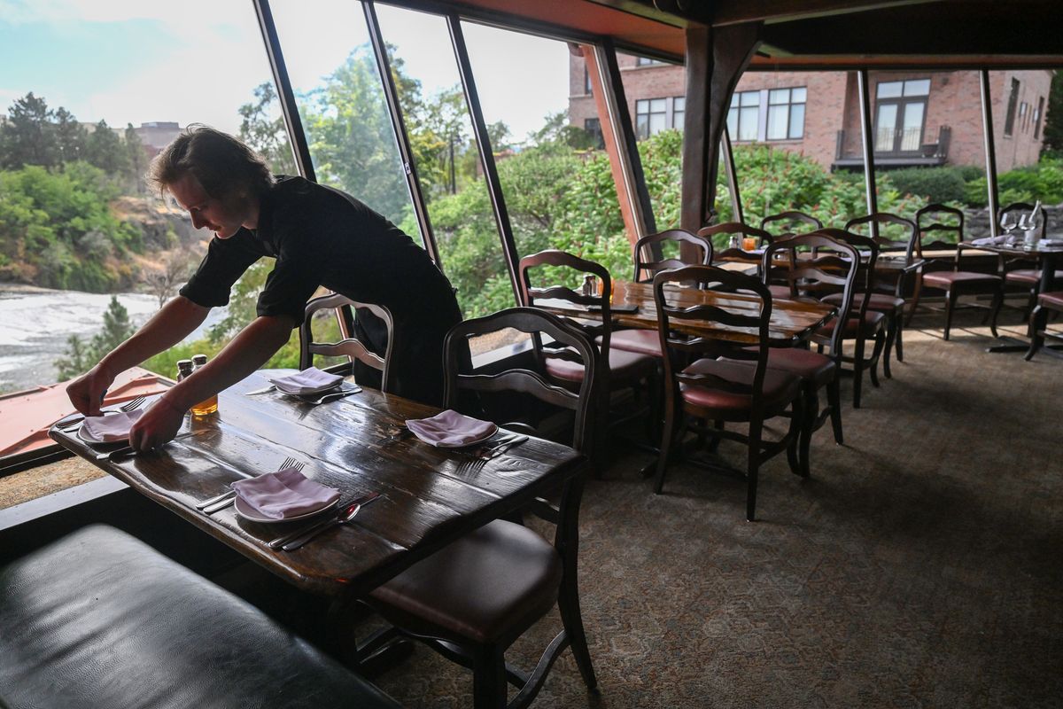 Server Jesse Becker prepares tables for dinner service in the outer dining room, which has scenic views of Spokane Falls from tableside at Clinkerdagger, the upscale restaurant in the historic Flour Mill. The restaurant, a Spokane institution, opened about the time of Expo ’74.  (Jesse Tinsley/THE SPOKESMAN-REVIEW)