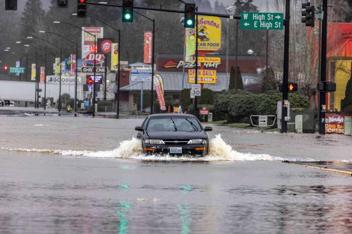 After driving past road closed signs a driver flows their way down Harrison Avenue Friday, Jan. 7, 2022, in downtown Centralia, Wash. The area is being flooded by the Skookumchuck River.  (Steve Ringman)