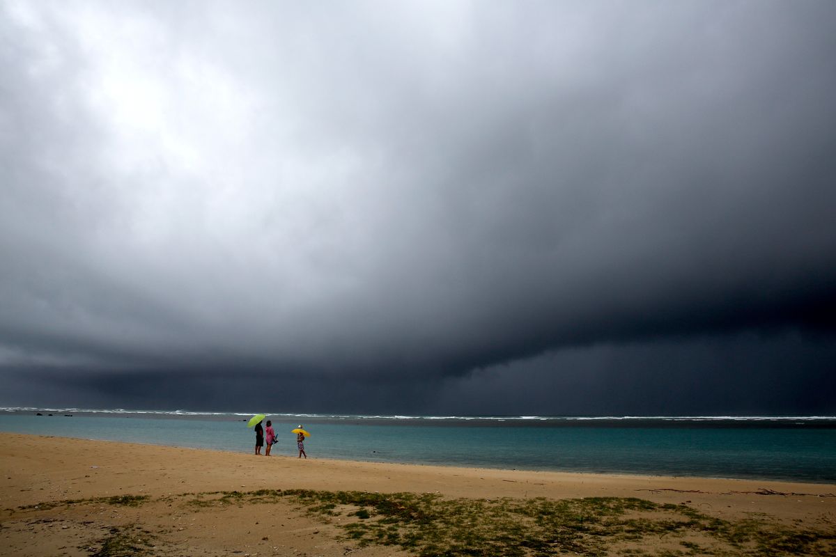 People hold umbrellas as it begins to rain on an otherwise empty beach in Honolulu on Monday, Dec. 6, 2021. A strong storm packing high winds and extremely heavy rain flooded roads and downed power lines and tree branches across Hawaii, with officials warning Monday of potentially worse conditions ahead.  (Caleb Jones)