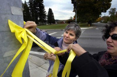 
 Mary DeLateur, left, and Cindy Guenther tie a yellow ribbon at Argonne and Upriver Drive in Spokane Valley. 
 (Liz Kishimoto / The Spokesman-Review)