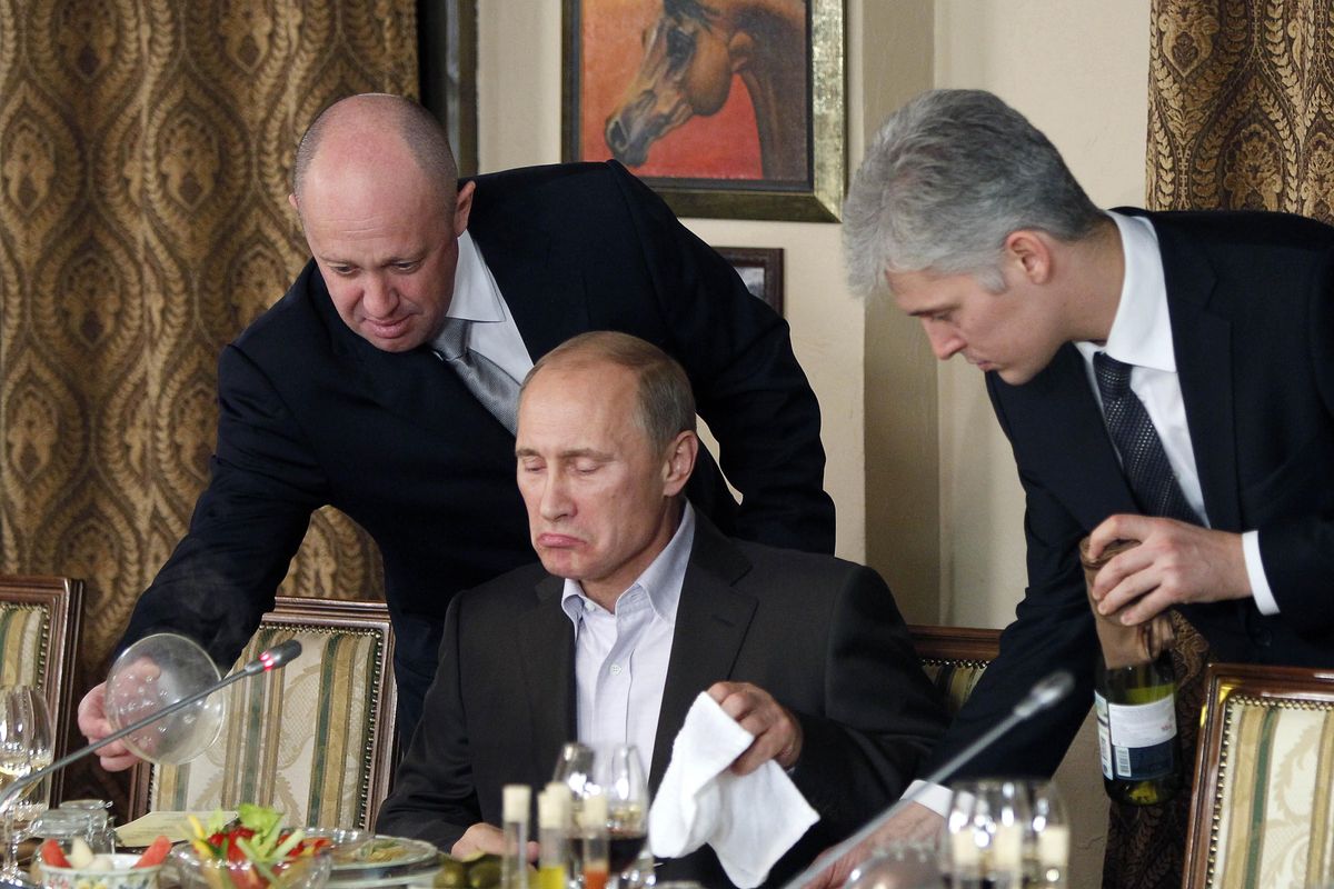 In this Friday, Nov. 11, 2011 file photo, businessman Yevgeny Prigozhin, left, serves food to Russian Prime Minister Vladimir Putin, center, during dinner at Prigozhin