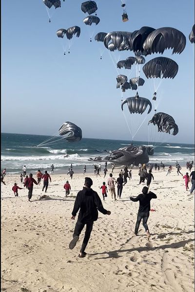 This image grab from an AFPTV video shows Palestinians running toward parachutes attached to food parcels, air-dropped from U.S. aircrafts on a beach in the Gaza Strip on Saturday.  (AFP/Getty Images North America/TNS)