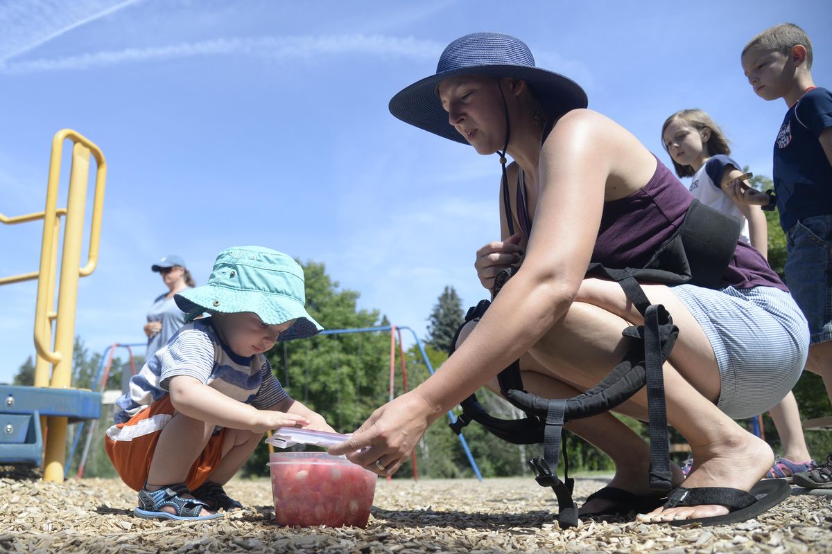 Elisabeth Lindsey, right, opens a snack of watermelon balls for her son Roland, left, at a play date Friday at Polly Judd Park for moms and kids of Attachment Parenting Village, a Facebook group that focuses on the issue of bonding with and raising their young children. (Jesse Tinsley / The Spokesman-Review)