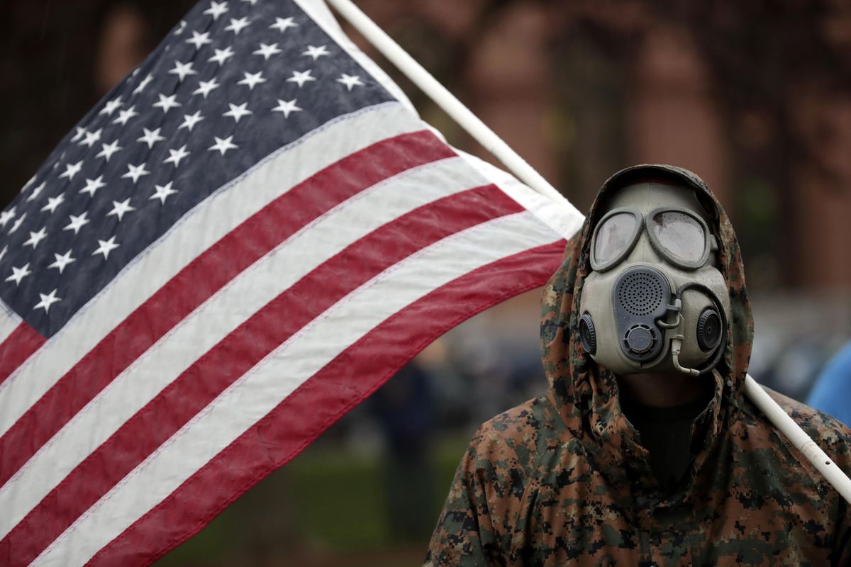 A protester wears a gas mask and carries an American flag during a rally in response to Michigan’s coronavirus stay-at-home order at the State Capitol in Lansing, Mich., Thursday, May 14, 2020. (Paul Sancya / AAssociated PressP)