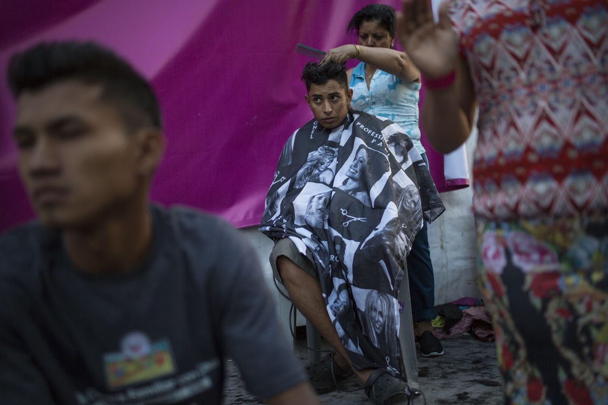 Honduran migrant Luis Fernando Barahona looks at an ongoing Catholic mass while a hairdresser cuts his hair at a shelter at the Jesus Martinez stadium, in Mexico City, Wednesday, Nov. 7, 2018. (Rodrigo Abd / Associated Press)