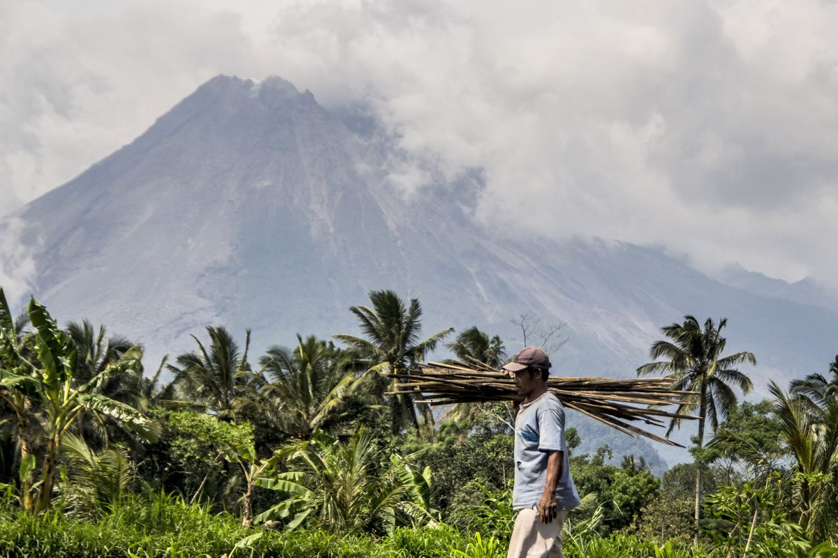 A farmer walks on his field as Mount Merapi is seen in the background in Sleman, Indonesia, Thursday, Nov. 5, 2020. Indonesian authorities raised the danger level for the volatile Mount Merapi volcano on the densely populated island of Java on Thursday and ordered a halt to tourism and mining activities.  (Slamet Riyadi)