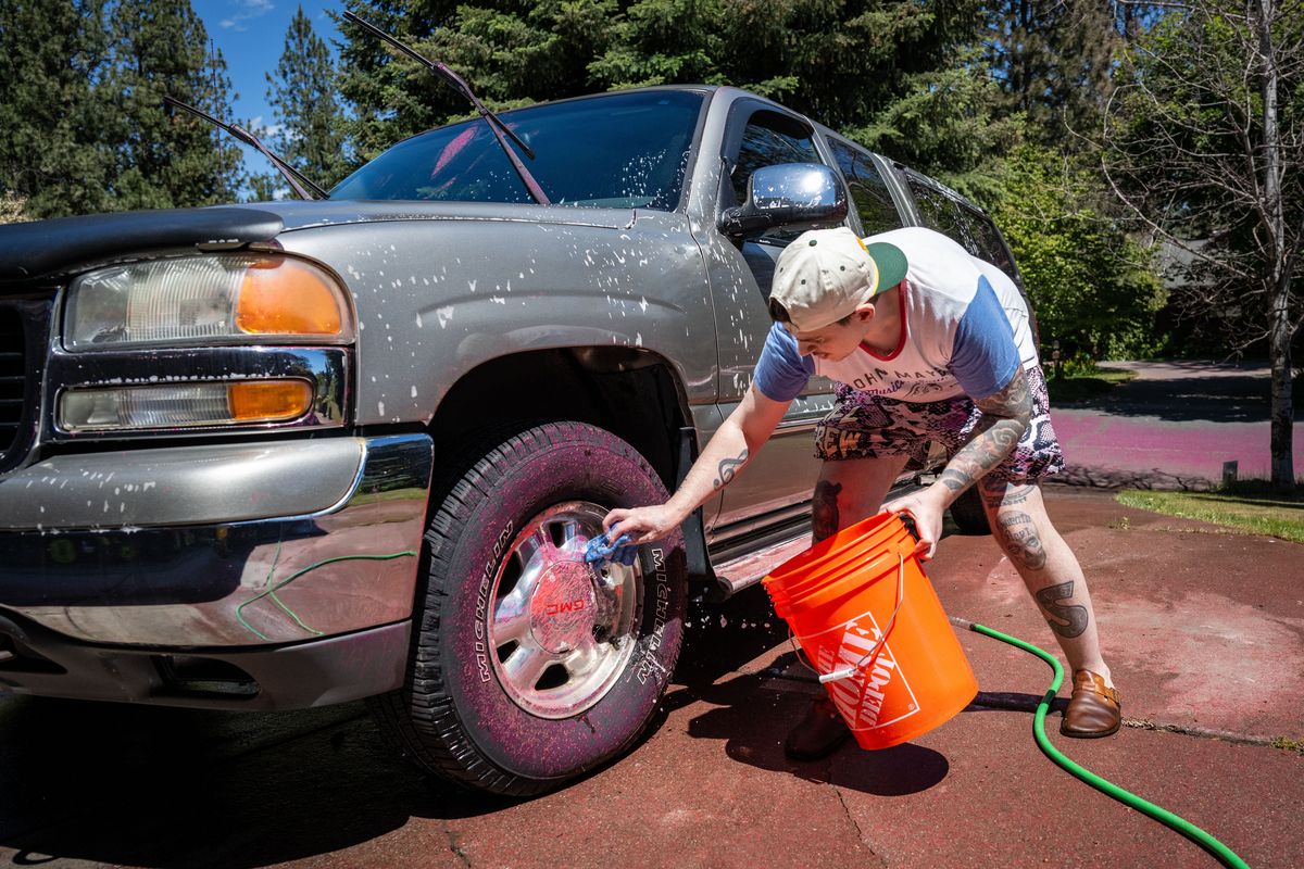 After just returning to his house Thursday, Jordan Walsdorf washes off red fire retardant clinging to a vehicle parked in his driveway on Vista Circle near Spokane Valley. (COLIN MULVANY /THE SPOKESMAN-REVIEW)