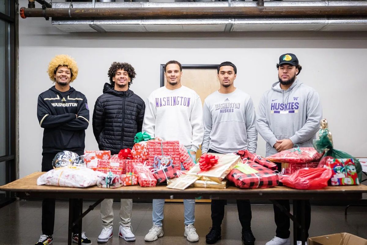 Washington football players Rome Odunze, left, Jalen McMillan, Bralen Trice, Alphozo Tuputala and Troy Fautanu pose with their wrapped gifts during the Montlake Futures event with the Forgotten Children’s Fund on Dec. 8 at the organization’s North Pole warehouse in Kent, Wash. The players volunteered to wrap presents for the Forgotten Children’s Fund.  (Emma Ottosen/Seattle Times)