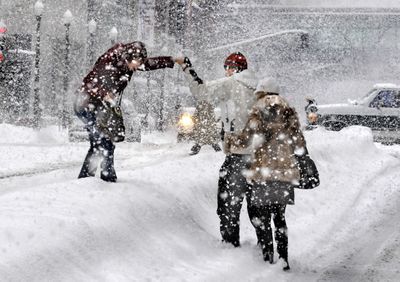 From left, Olga Major, Andrei Galynine and Yualiya Burdeyna make the leap across a berm in the middle of the 900 block of West Riverside Avenue during a  snowstorm  Monday.   (CHRISTOPHER ANDERSON / The Spokesman-Review)