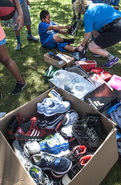 Spokane police Officer Jennifer DeRuwe assists Jonathan Gonzalez in trying a new pair of shoes donated by the community to the Spokane Police Athletic League, Aug. 2, 2016, at Cannon Park in the West Central Neighborhood. The children can use the footwear for PAL activities such as baseball, soccer and running. (Dan Pelle / The Spokesman-Review)