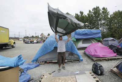 Ion Gardescu lifts up his tent to shake debris out of it as he breaks camp Thursday at the homeless tent camp named “Nickelsville”  in south Seattle.  (Associated Press / The Spokesman-Review)