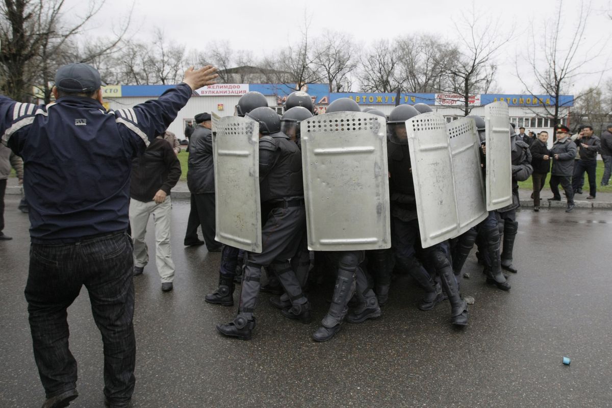 Kyrgyz police huddle together for protection, as they come under attack from protestors near the main government buildings in Bishkek, Kyrgyzstan, on Wednesday. Police in Kyrgyzstan opened fire on thousands of angry protesters.  (Associated Press)