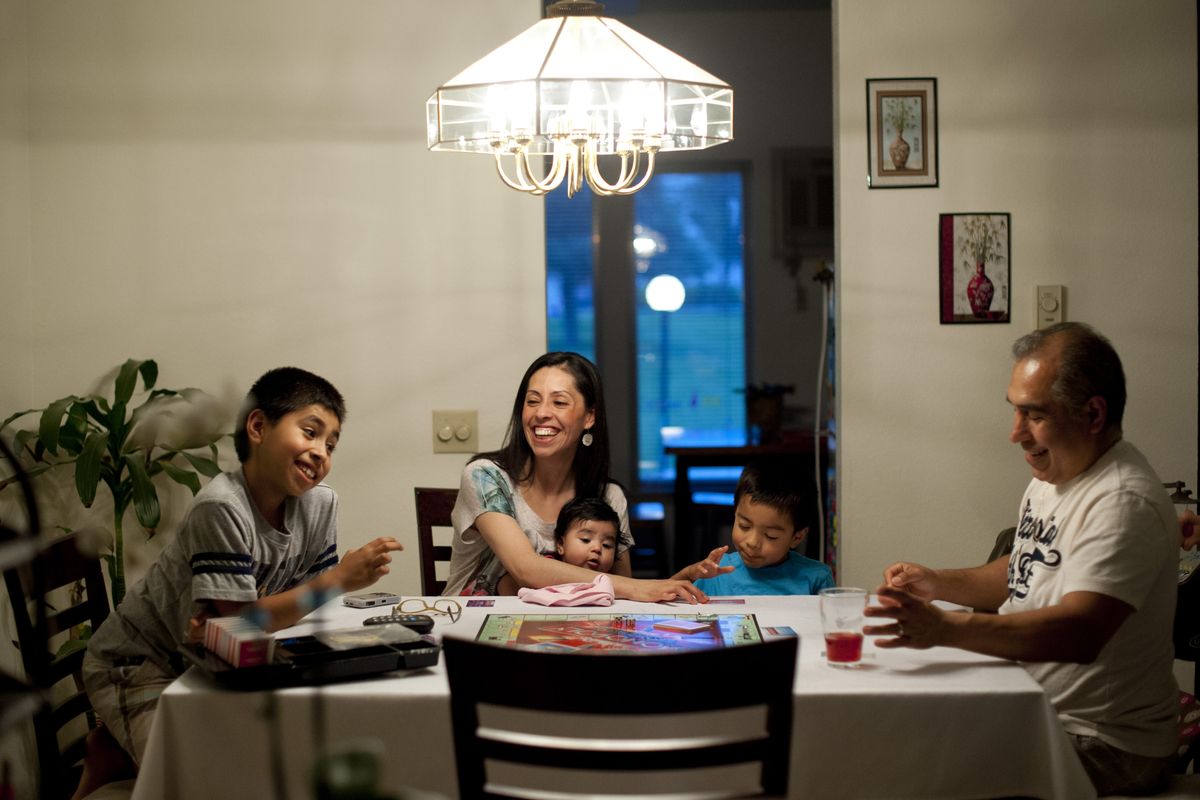 Julian Arias, 9, left, plays Monopoly with his mother, Alejandra, father, Jose, and brother, Jared, 4, while 4-month-old Alyssa watches on June 28 in their north Spokane home. The Ariases place emphasis on Catholic education, values and family unity. (Tyler Tjomsland)