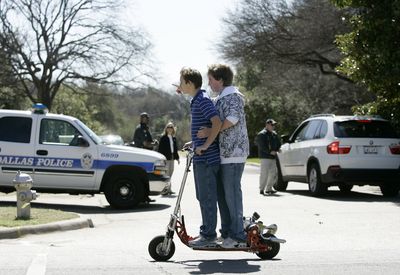 Two boys drive by on a  scooter as Dallas police and Secret Service agents maintain a checkpoint near former President George W. Bush’s new residence in Dallas on Friday. (Associated Press / The Spokesman-Review)