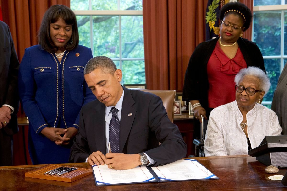 President Barack Obama signs a bill designating the Congressional Gold Medal commemorating the lives of the four young girls killed in the 16th Street Baptist Church Bombing of 1963, Friday, May 24, 2013, in the Oval Office of the White House. Standing, from left are Rep. Terri Sewell, D-Ala., and Lisa McNair. Seated at right is Thelma "Maxine" Pippen McNair, the mother of Denise McNair. Maxine McNair, the last living parent of any of the children killed in the 1963 bombing of Birmingham