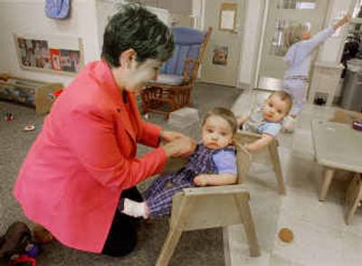 
Tracy Baroni Allmon fixes the outfit on one of her 7-month-old triplets, Spencer, as his brother, Luke, watches and their sister, Piper, 3, plays in the background on Tuesday at the Child Development Center at Bristol-Myers Squibb.
 (Associated Press / The Spokesman-Review)