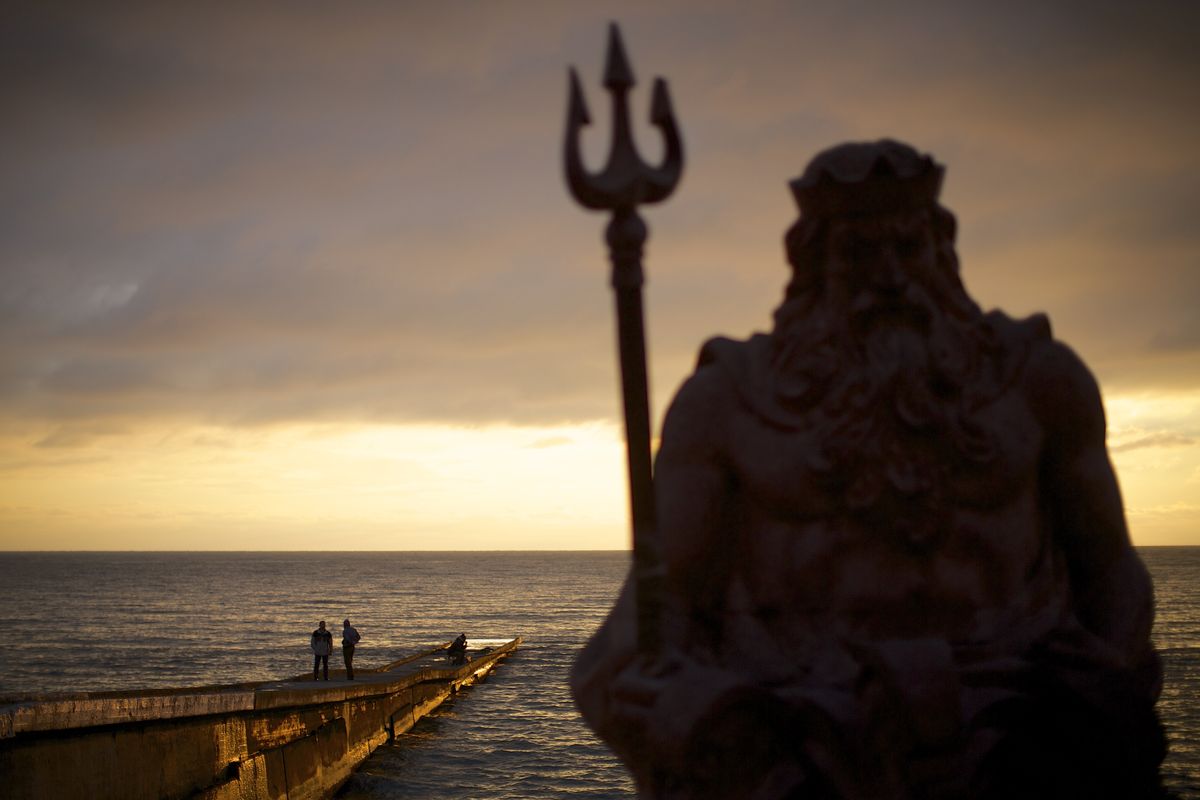 A statue of the ancient Roman god Neptune sits guard off the beach during the sunset on an embankment at Sochi, Russia. (Associated Press)