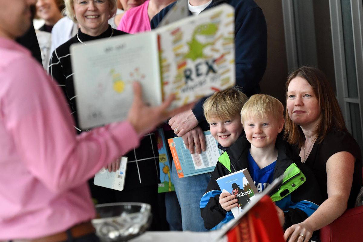 Nathan Moss, left, and his brother, Drew Moss, are held by their mother Jessie Moss as, Cody, father of Isaac Brincken, the Moss' second cousin, who at five-months-old succumbed to Complications with CHARGE syndrome, reads through one of Issas favorite books during a dedication of "Issac's Bookshelf" on Monday, Feb. 18, 2019, at Sacred Heart Hospital in Spokane, Wash. Isaac's Bookshelf was created in his memory to share the joy of reading with children who are in the hospital undergoing treatment for complex medical conditions. The bookshelf rolls around the unit visiting patients. (Tyler Tjomsland / The Spokesman-Review)
