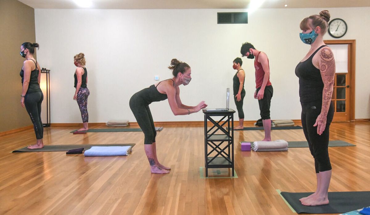 Shelley Enlow, owner and director of Ashtanga Yoga, center, begins her class Friday, Sept. 18, 2020, by connecting online with students and having in-person students practice social distancing.  (DAN PELLE/The Spokesman-Review)