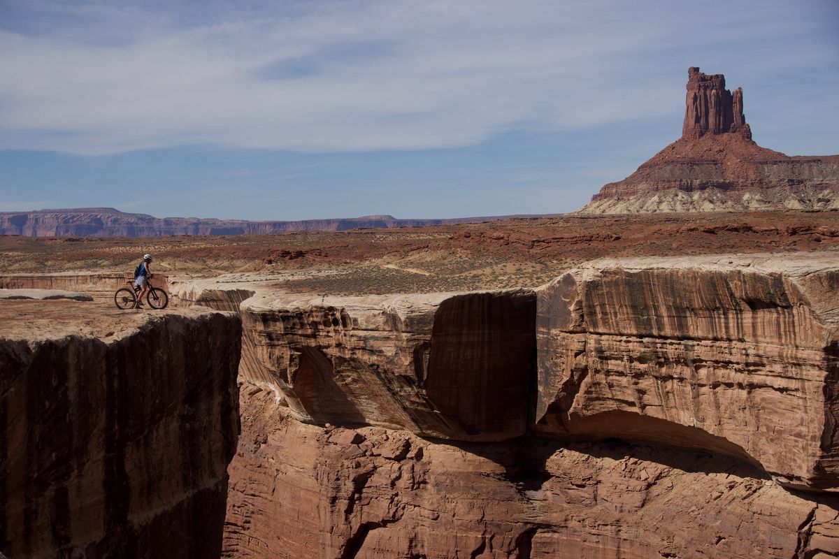 A mountain biker pauses at an overlook of Soda Springs Basin along the White Rim Road. The road is built mostly atop a dense layer of sandstone – visible at the bottom of the candlestick formation in the background – deposited 245 million to 286 million years ago.  (Photo for The Washington Post by John Briley)
