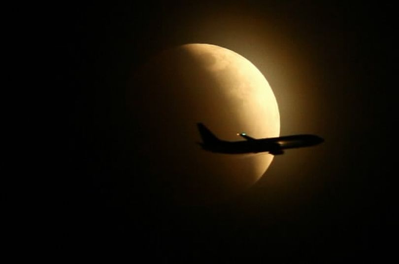 An airplane passes in front of a darkening moon as it becomes a total lunar eclipse on Wednesday, Feb. 20, 2008 in Seattle. (Joshua Trujillo / Associated Press)