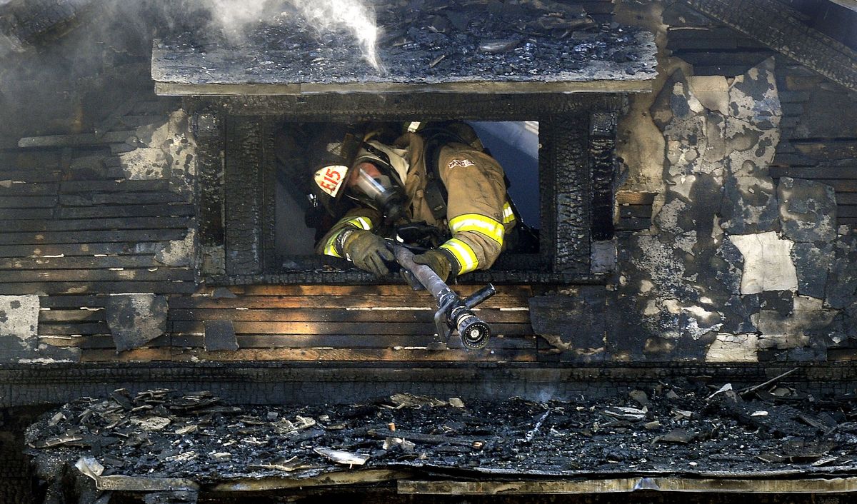 A Spokane firefighter from Station 15 squeezes through a second-floor window to gain position to spray hot spots on the home  on Friday. The house was engulfed when firefighters arrived.  (Dan Pelle / The Spokesman-Review)