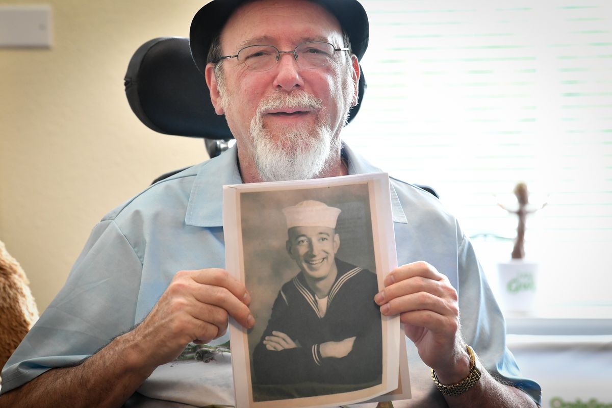 John Derrick poses with an image of his father Edwin Derrick on 2022, at his home in Spokane.  (Tyler Tjomsland/The Spokesman-Review)