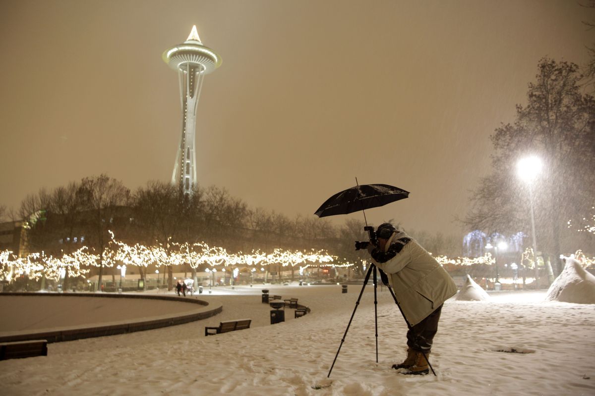ORG XMIT: WATW201 Photographer Anthony Evora uses an umbrella to keep falling snow off of his camera Saturday, Dec. 20, 2008, as he takes pictures of winter scenes near the Space Needle in Seattle. The winter beauty was also expected to bring hardship to the area Saturday night as high winds, freezing rain and heavy snow were forecast for most of Western Washington. (AP Photo/Ted S. Warren) (Ted Warren / The Spokesman-Review)