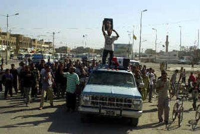 
An Iraqi man holds up a photo of Shiite cleric Muqtada al-Sadr as he stands next to a coffin on the top of a truck during a funeral procession earlier this month in Baghdad's Sadr City neighborhood Wednesday where the dead man, Muthana Hafiz, was killed the night before during clashes with U.S. troops. 
 (Associated Press / The Spokesman-Review)